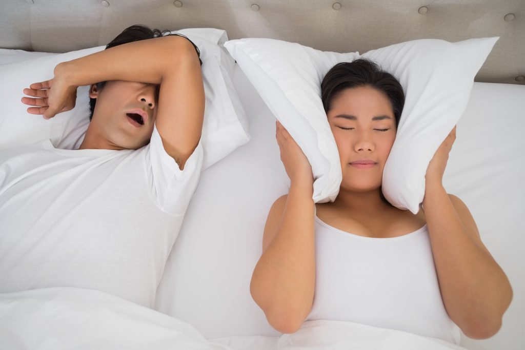 annoyed woman covering her ears with pillows block out snoring